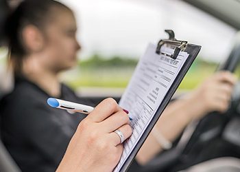 Teen Girl Learns Driver's Education in Car with Adult  woman using clipboard,  Young Teen Girl Doing Driving Exam with female Examiner while holding Checklist during bright day.