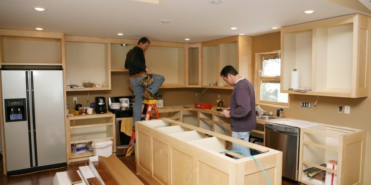 Cabinet maker installing custom made kitchen island and cabinets, while electrician installs in-cabinet lighting. 
Very shallow DOF quickly drops off to nice soft focus.